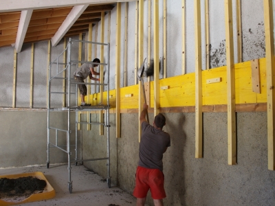 Remplissage entre support et banches en tassant légèrement le long des banches et autour de l'ossature, doublage isolant épais en Béton de Chanvre en cours de réalisation, isolation de murs